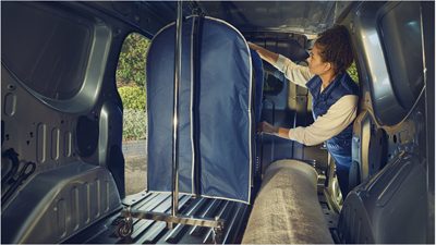 A woman moving a large piece of luggage in the back of a Renault Express Van.