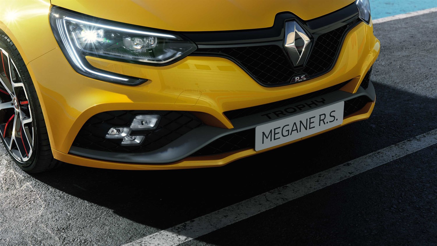 A front corner view of the Renault MEGANE R.S. branding displayed in the yellow-colored version
